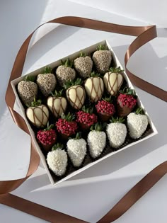 a box filled with chocolate covered strawberries on top of a white table next to a brown ribbon