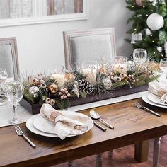 the table is set for christmas dinner with pine cones and greenery