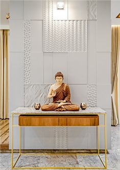 a buddha statue sitting on top of a wooden table in front of a white wall