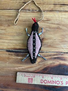 a small beaded bug sitting on top of a wooden table next to a ruler