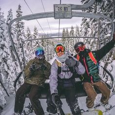 three snowboarders sitting on a ski lift in the middle of a snowy forest