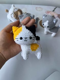 a hand holding a tiny crocheted cat ornament in front of three other cats