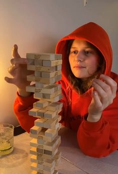 a girl in a red hoodie is playing with a stack of wooden blocks on the table