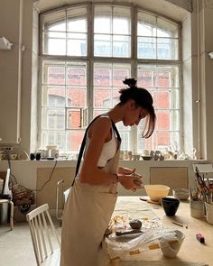 a woman standing in front of a window making food on a table with bowls and utensils