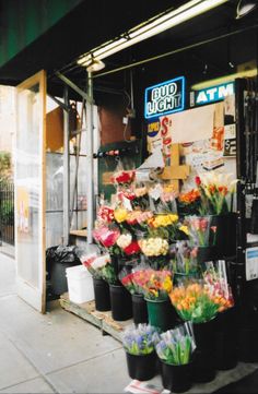 a bunch of flowers that are on display in front of a storefront with an atm sign