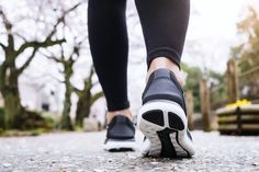 a person wearing black and white shoes walking down a street with trees in the background