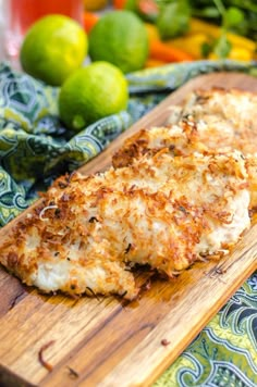 two pieces of chicken on a wooden cutting board next to lemons and limes