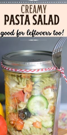 a jar filled with pasta salad sitting on top of a wooden table next to vegetables