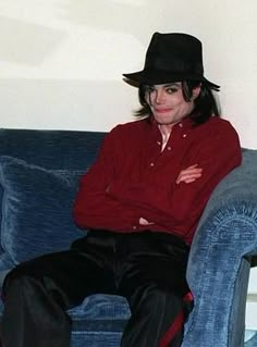 a man sitting on top of a blue couch wearing a black hat and red shirt