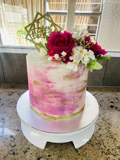 a pink and white cake sitting on top of a counter next to a vase filled with flowers