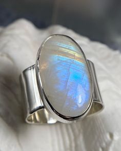 Large Rainbow Moonstone Cabochon bezel set in sterling silver on a shiny, minimalistic wide band. Ripple shoulder details accentuate this lovely oval setting. 100% handmade in Los Angeles.  Size: 9.5 Inner ring diameter: 19.6 mm Tip: Wider bands like this usually fit best a half size above your usual ring size. Compare this measurement with your favorite rings for accurate fit! Rainbow moonstone has much history and energy properties associated to it and is said to bring good fortune. See for yourself, this ring will surely bring you joy at every glance. Enjoy seeing the rainbow flash as light shines at different angles. Handmade in Los Angeles with free shipping on all US orders!  Thank you for shopping Samama Jewelry, visit my shop to see the rest of my unique jewelry designs. Discover y Modern Oval Moonstone Ring For Formal Occasions, Modern Oval Cabochon Moonstone Ring, Minimalist Sterling Silver Cabochon Moonstone Ring, Modern Oval Moonstone Jewelry, Modern Moonstone Ring With Oval Cabochon, Modern Moonstone Ring With Large Stone, Modern Oval Cabochon Opal Ring As Gift, Oval Modern Moonstone Ring With Bezel Setting, Modern Moonstone Ring With Oval Bezel Setting