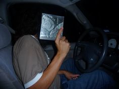 a man sitting in the driver's seat of a car holding up a book