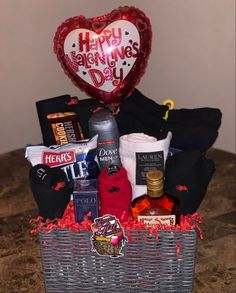 a heart shaped balloon sitting on top of a basket filled with food and wine items