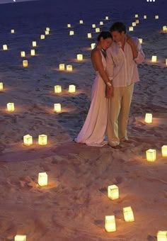 a man and woman standing in the sand with many lit candles