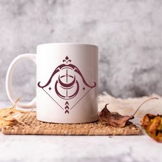 a white coffee mug sitting on top of a bamboo mat next to leaves and an autumn leaf