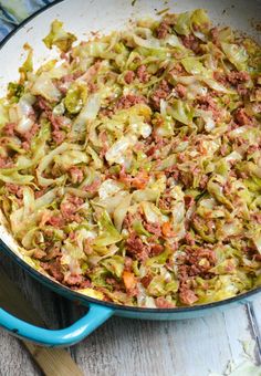 a blue skillet filled with cabbage, meat and cheese on top of a wooden table