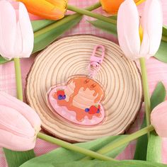 a pink keychain with a cake on it sitting next to tulips