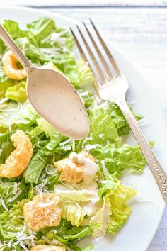 a white plate topped with salad covered in dressing next to a fork and spoon on top of it