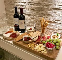 a wine bottle and two bottles of wine on a table with cheeses, crackers, grapes and breadsticks