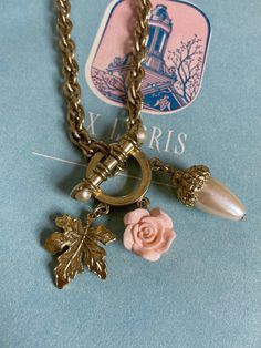 Very gorgeous and classically mid century golden toned toggle front necklace. Large ornately molded toggle with pearl capped ends and large circular closure. Three fauna charms of a golden toned, highly detailed leaf, an acrylic rose in a peachy pink, and pearl golden toned acorn. The perfect combination of charms that allows this piece to fit into your wardrobe during any season. Suspended on a golden toned Singapore style chain with some of the links displaying etched texture. Weighty and qual Singapore Style, Acrylic Rose, Toggle Necklace, Peachy Pink, Chain Lengths, Charm Necklace, Jewelry Necklaces, Charms, Mid Century