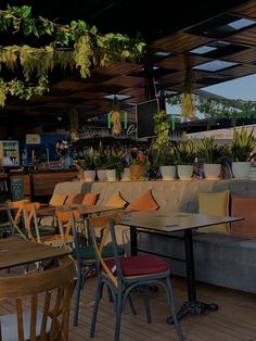 an outdoor seating area with tables, chairs and potted plants hanging from the roof