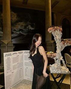 a woman in a black dress standing next to a table