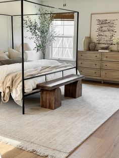 a bedroom with a canopy bed, bench and dressers in the corner next to it