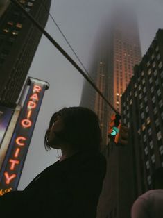 a woman standing in the middle of a street next to tall buildings and traffic lights