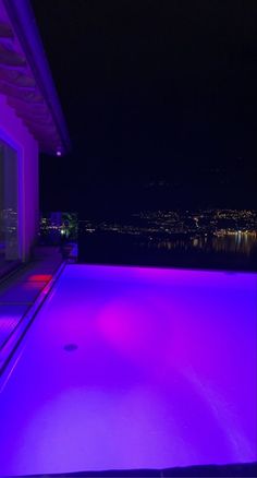 an empty swimming pool at night with the city lights in the background and purple lighting