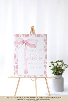 an easel with a pink bow on it next to a potted plant