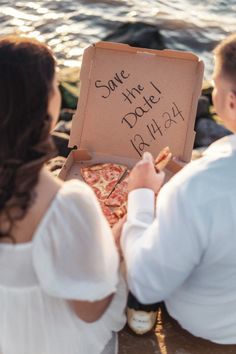 a man and woman sitting next to each other on the beach with pizza in front of them