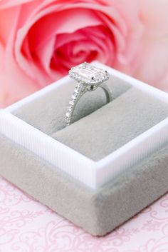 an engagement ring sits in a box next to a pink rose