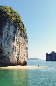 people are swimming in the clear blue water next to an island with two large rock formations