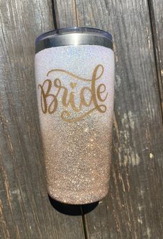 the bride glitter tumbler cup is sitting on top of a wooden table next to a fence