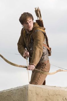 a young man with an arrow and bow on top of a sand structure in the desert