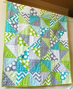 a green and blue quilt hanging on the wall