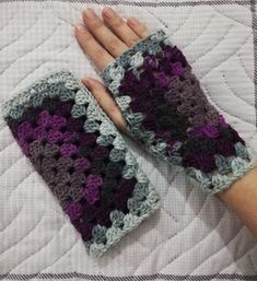 a woman's hand is holding two crocheted gloves on top of a quilt