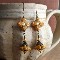 Lovely Czech glass flower earrings in a pretty butternut orange color. For these, I chose a pair of beautiful and unique four-pointed flower beads, and paired them with bell flowers in a similar shade, which I hung below them. Both beads are a beautiful butternut orange with gold accents. I paired them with antiqued brass and some small orange beads to accent their beauty, then hung them from simple French earwires. These earrings measure just over 2 1/2 inches, or about 6.5 cm, including the French earwires. (They are also available with leverback earwires if you prefer, which are a similar length to the French ones.) All of the beads are Czech glass, and all of the metal is antiqued brass or antiqued brass-plated. Knitting Moodboard, Czech Beads Jewelry, Glass Flower Earrings, Bell Flowers, Earring Inspiration, Earrings Ideas, Flower Dangle Earrings, Eyeliner Makeup, Steampunk Accessories