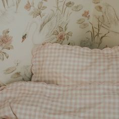 an unmade bed with a pink and white checkered comforter next to a floral wallpaper