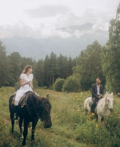 two people are riding horses through the woods