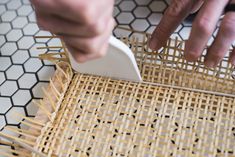 a person using a brush to clean a wicker basket on a tiled floor with black and white hexagonal tiles in the background