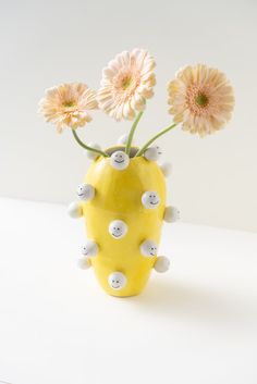 a yellow vase filled with flowers on top of a white table