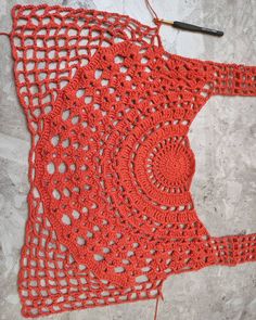 an orange crocheted doily on the ground next to a knitting needle and thread