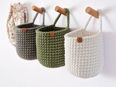 three crocheted baskets hanging from hooks on a white wall, one is green and the other is brown