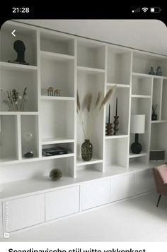 a living room filled with lots of white bookshelves next to a pink chair