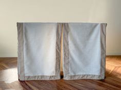 two white curtains sitting on top of a hard wood floor