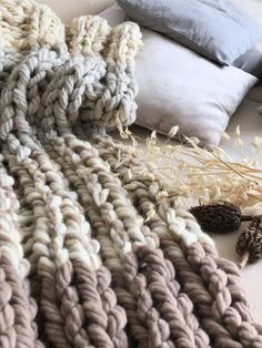 a knitted blanket laying on top of a bed next to pillows and dried flowers