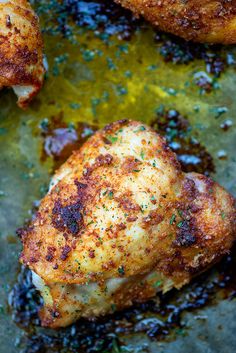 two pieces of chicken sitting on top of a pan covered in oil and seasoning