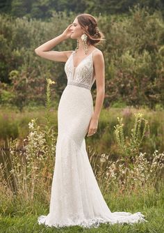 a woman in a wedding dress standing in the grass with her hand on her head