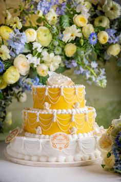 a yellow and white wedding cake sitting on top of a table next to blue flowers